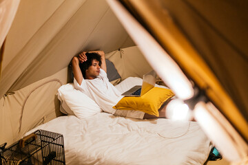 latin man watching a series on the computer lying on the bed in a tent