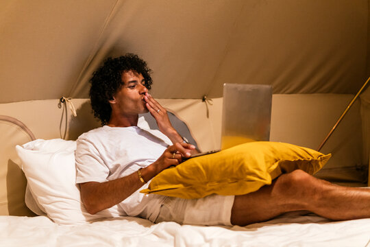 latin man blowing a kiss on a video call lying on the bed in a tent