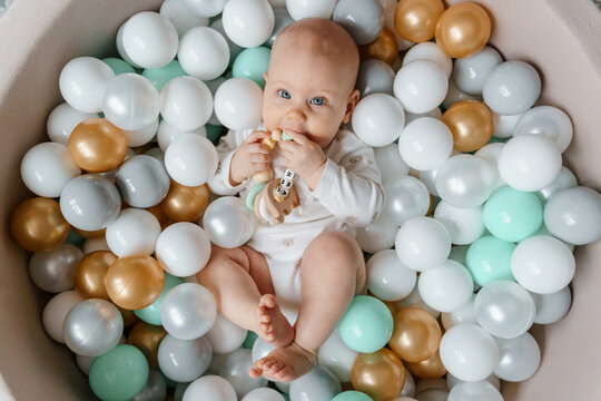 6 month old baby lies in the pool with balls and gnaws teether