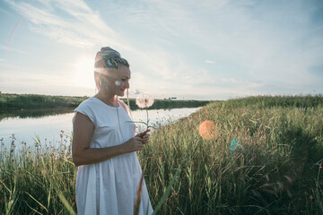 girl with multicolored braids enjoys summer, face sideways, dandelion