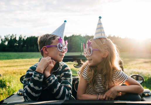 girl & boy sat in a convertible car with party hats and glasses