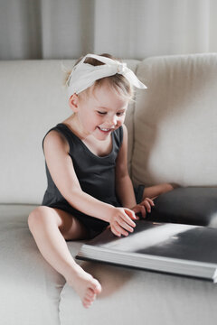 Girl 2 years old sits on the couch and looks at a huge book, laughs