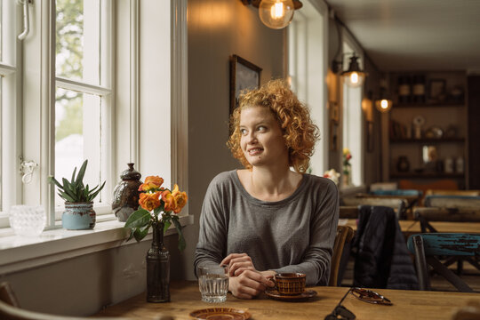 Happy young woman sitting at table with coffee