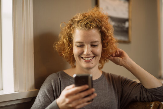 Happy young woman sitting in chair and reading text messages