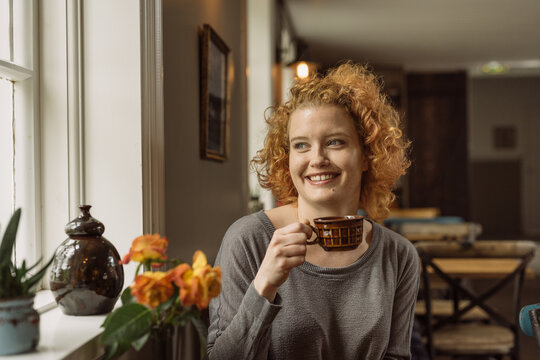 Cheerful young woman sitting at table with cup of coffee in cafe
