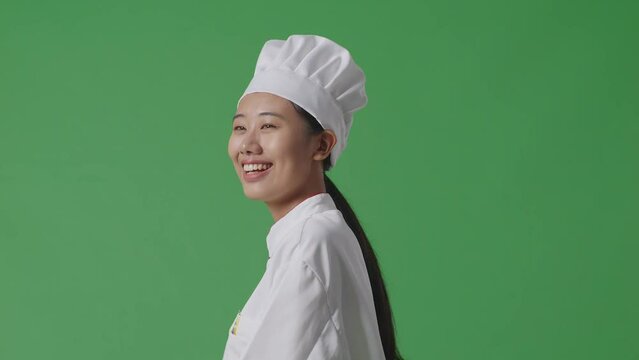 Side View Of Asian Woman Chef Walking And Looking Around In The Green Screen Background Studio
