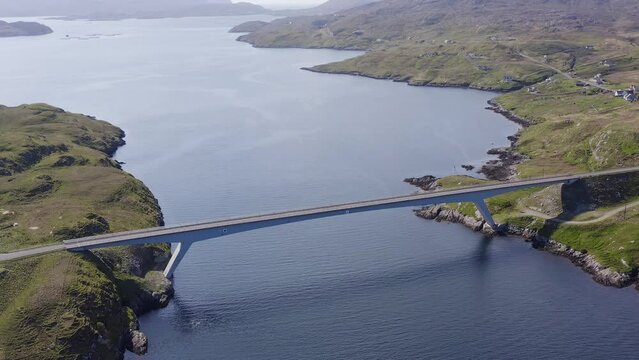 Tilting, wide angle drone shot of the bridge connecting the Isle of Scalpay to the Isle of Harris on the Outer Hebrides of Scotland. The town of Tarbert and the surrounding bay is visible.