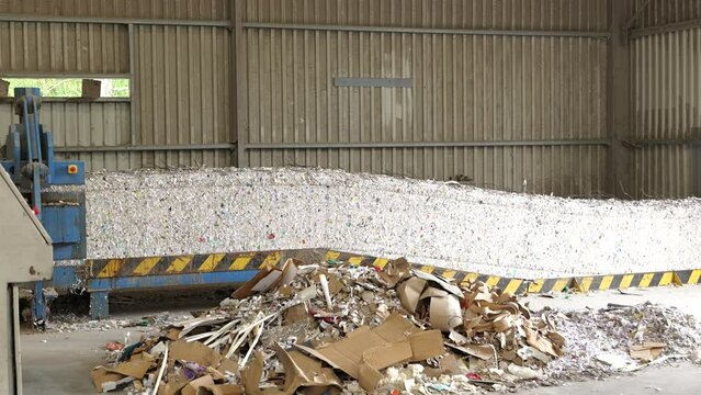 Bales of shredded paper exiting baler, moving on conveyor in recycling center.