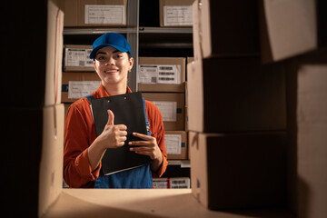 Happy warehouse female worker holding clipboard and showing thumbs up gesture