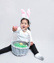 A wide-smiling girl with rabbit ears on her head and painted eggs in her hands. on a light background.