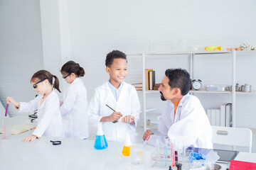 Cheerful group of Multicultural primary school students wearing lab coats studying with Indian...