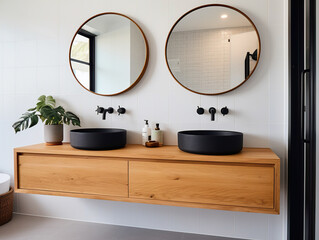 Clean ensuite bathroom with wall mounted timber vanity and black sink and pill shaped mirrors.	