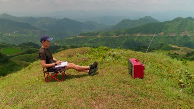 young man watches television in a relaxing outdoor atmosphere, taking notes on an important broadcast