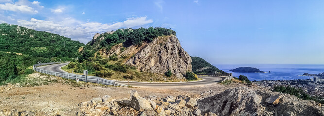 Large-format panorama of the M2.3 highway around the cliff against the backdrop of the Adriatic Sea with the Sveti Nikola island and Budva town on the coast, Montenegro. Beautiful scene of mountains