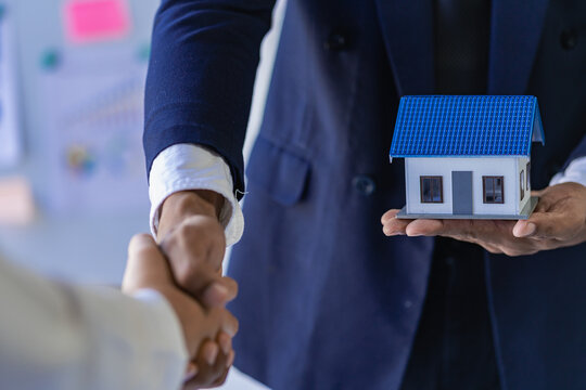 Real estate agents shake hands with business clients and present current home purchases and rentals. The sales representative offers a house project. Close-up pictures