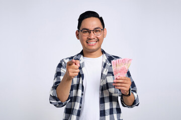 Successful financial planning. Smiling young Asian man in casual shirt holding money and pointing finger at camera isolated on white background