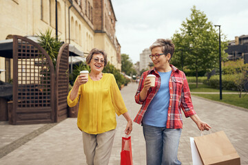 Smiling stylish senior women meeting outdoors, drinking coffee and shopping in the city centre