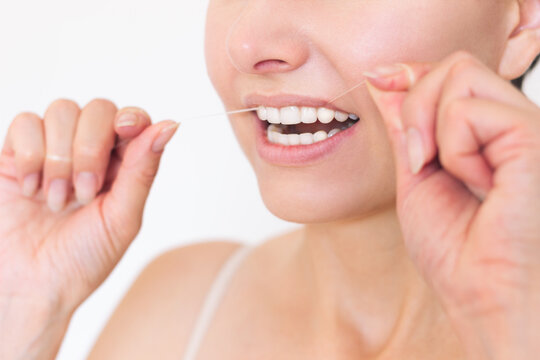 A close-up photo of a young Caucasian woman who uses dental floss to clean her teeth and interdental space. Oral hygiene and maintenance of dental health.