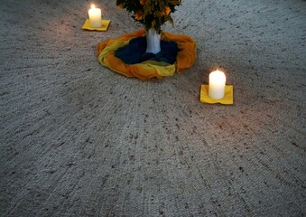 Dekoration in Kirche mit zwei weißen brennenden Kerzen vor weißer Vase mit Blumenstrauß auf...