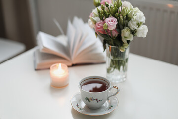 Romantic still life, a bouquet of roses in a vase, a cup of tea and an book on white table