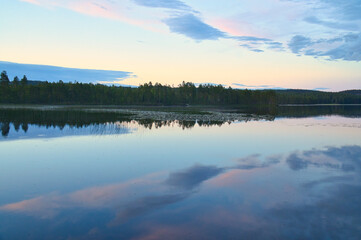 Fototapeta na wymiar Calm lake in Sweden at blue hour sunset. Clouds reflected in the water. Swimming