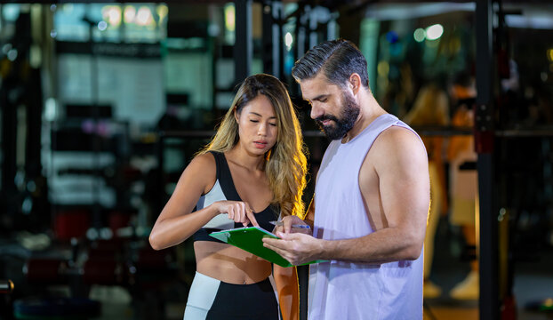 Gym customer is getting advice and suggestion from her personal trainer for exercising plan program and getting her evaluation chart from sample blood test for her workout progress
