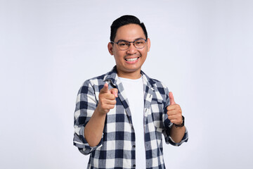 Hey, you! Cheerful young Asian man in casual shirt pointing index finger at camera isolated on...