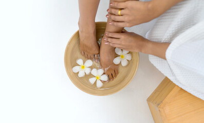 Female feet soaked in a bowl filled with water and flower petals, a depiction of relaxation and luxurious self-care.