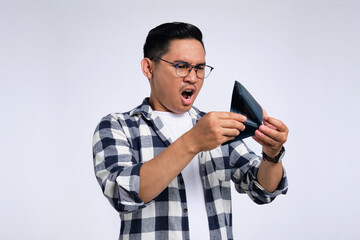 No money. Surprised young Asian man in casual shirt looking at empty wallet, having financial problems isolated on white background