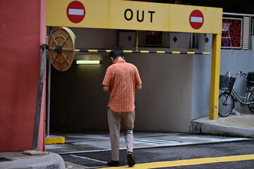 A man walks the wrong way into a parking garage in Singapore. Two stop signs on yellow background.