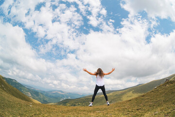 Strong women, new challenges - concept. A young woman with her hands raised to the sky in a beautiful mountain landscape.