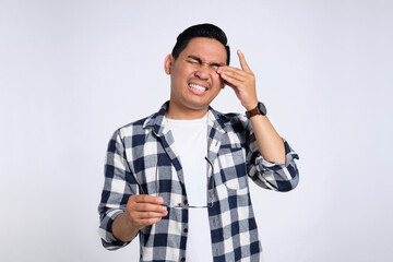 Tired young Asian man in casual shirt taking off glasses, feeling eye strain after work isolated on white background