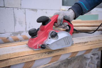 A plane on a rough wooden board in the hands of a master wearing gloves. Planer for woodworking and interior design