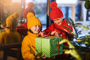 Happy children open gift boxes near the Christmas tree. Wonderful snowy winter background.