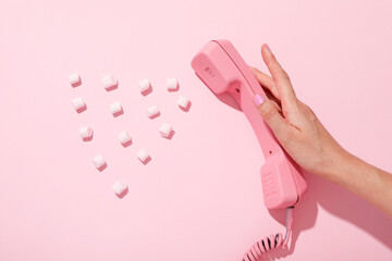 Vintage phone in female hand and marshmallow on pink background, space for text