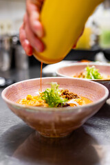chef cooking Asian noodle soup, ramen with chicken, tofu, vegetables and egg in bowl