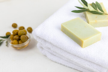 Obraz na płótnie Canvas Natural bar of soap with olive oil extract on white textured wood. Pieces of green nourishing soap and olive berries. Body care and spa concept. Place for text.Copy space.Flat lay