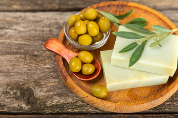 Natural bar of soap with olive oil extract on brown textured wood. Pieces of green nourishing soap and olive berries. Body care and spa concept. Place for text.Copy space.Flat lay
