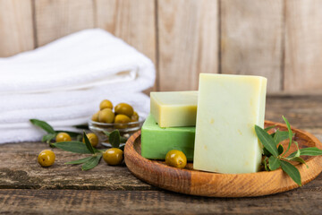 Natural bar of soap with olive oil extract on brown textured wood. Pieces of green nourishing soap and olive berries. Body care and spa concept. Place for text.Copy space.Flat lay