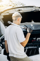 Torque wrench for car repair in the hand of an auto mechanic, which inspects the hood of the car,...
