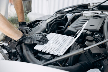 Computer diagnostics of the car. Assessment of the condition of the engine and other car parts. A man evaluates the condition of a car using a computer. Work in a car repair shop, service, garage.