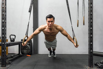 Fototapeta premium Athlete exercising on gymnastic rings in a well-equipped, modern gym. The man displays strength and determination, his muscles ripple with exertion.