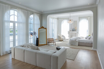 cozy bright apartment with huge panoramic windows with sunlight. bedroom in white and beige tones with fireplace and soft armchair. stylish living room with log coffee table and large white sofa