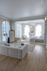 cozy bright apartment with huge panoramic windows with sunlight. bedroom in white and beige tones with fireplace and soft armchair. stylish living room with log coffee table and large white sofa