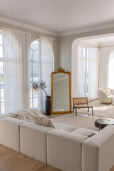 cozy bright apartment with huge panoramic windows with sunlight. bedroom in white and beige tones with fireplace and soft armchair. stylish living room with log coffee table and large white sofa