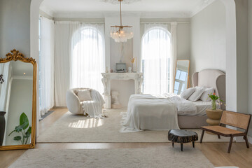 a gentle cozy bright apartment with huge panoramic windows with sunlight. bedroom in soft beige tones with a fireplace and a comfortable stylish upholstered armchair and bed