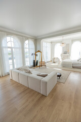 cozy bright apartment with huge panoramic windows with sunlight. bedroom in white and beige tones with fireplace and soft armchair. stylish living room with log coffee table and large white sofa