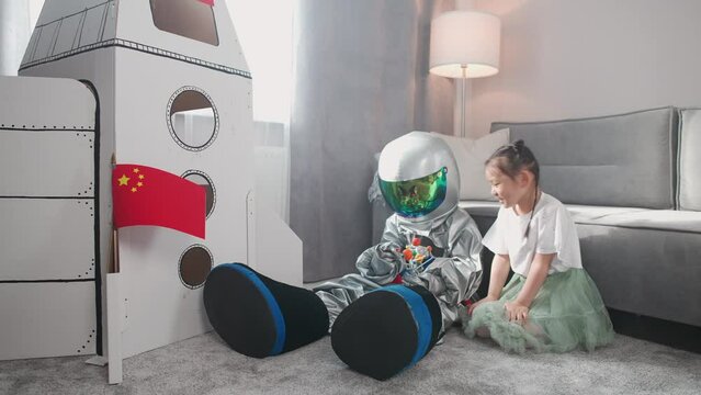 Asian kids play in the living room at home, a boy in an astronaut costume sitting on the floor with her sister, kids playing with a toy model of the solar system.