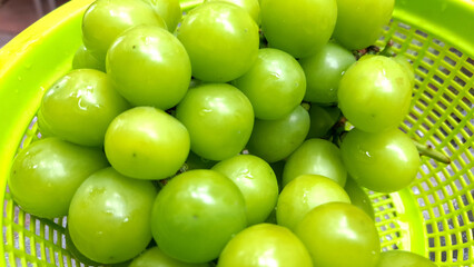 Image of fresh green muscat grapes placed in a green plastic basket