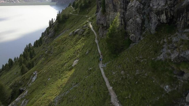 view from drone mountain path for hiking and walking in nature in Valmalenco valley italian Alps , Sondrio, Italy ,  Alpe Gera dam - sports couple run off road in the mountains